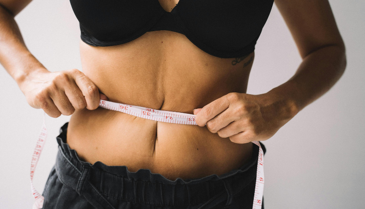 woman measuring her stomach with a tape measure