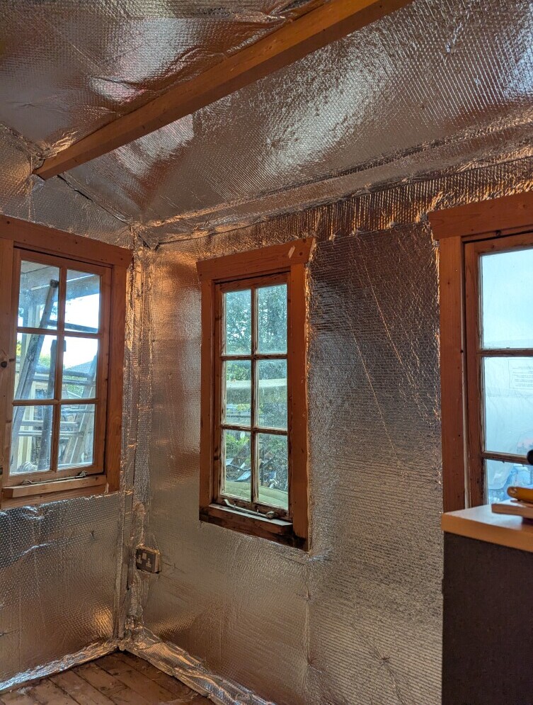 the interior of a wooden shed showing foil insulation pinned to the walls