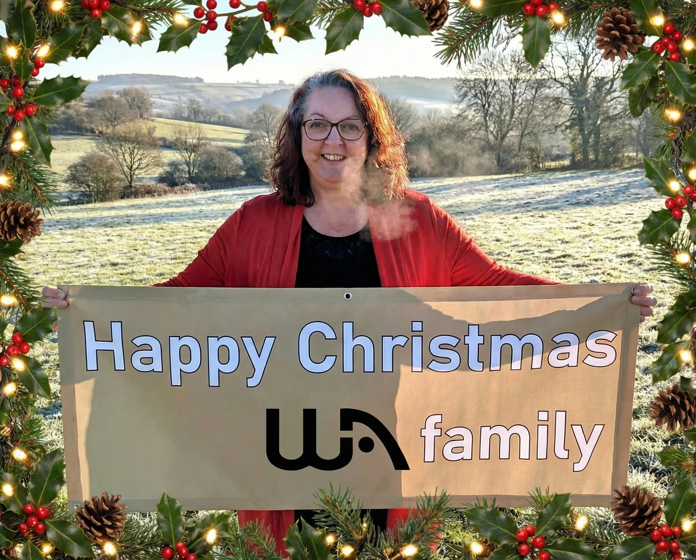 a woman holidng a banner saying "Happy Christmas WA family" - she is standing in a field with a Christmas border around the photo