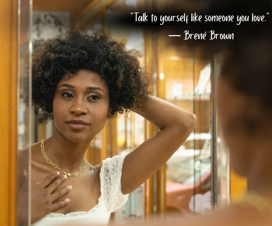 Young black woman looking at herself in the mirror with text: “Talk to yourself like someone you love.” — Brené Brown