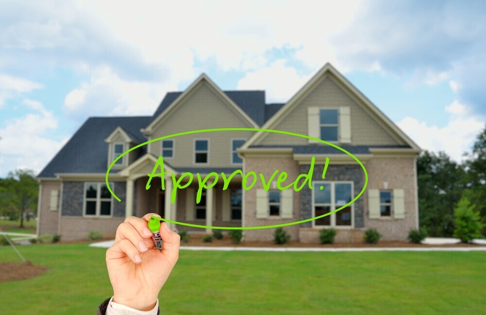 Image of a beautiful home in the background of a hand writing Approved signifying the the processes of buying a house and land is complete.