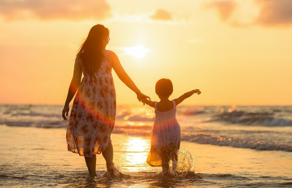 mother with young daughter walking on beach