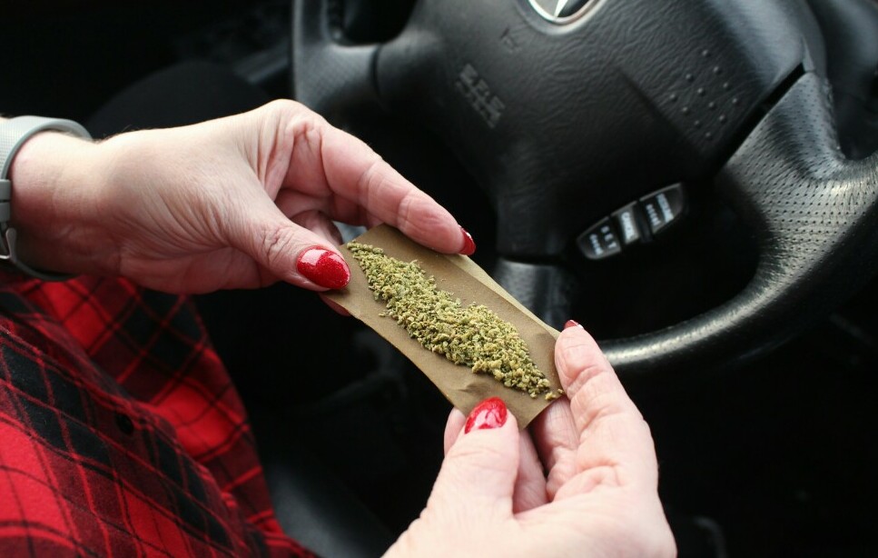 woman rolling a joint in the driver's seat of her car