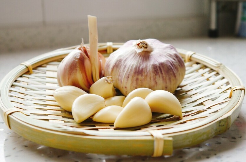 A bowl of fresh garlic in the middle of a woven plate