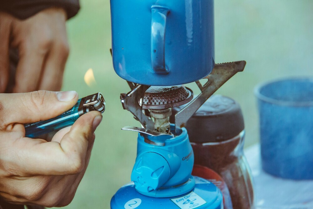 Hiker lighting a camping gas stove with a blue cup placed on top ready for a brew