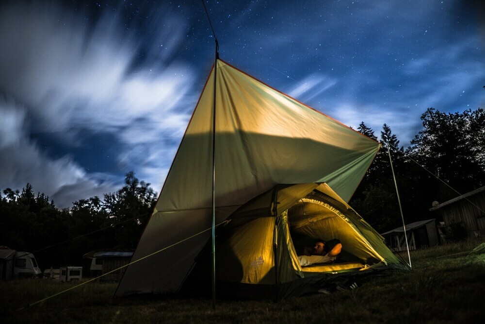 Hiker laying in his tent with the door open and a tarp stretched out over the top