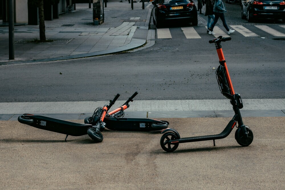 Three electric scooters in the city two on their side with a view of a zebra -crossing in the background