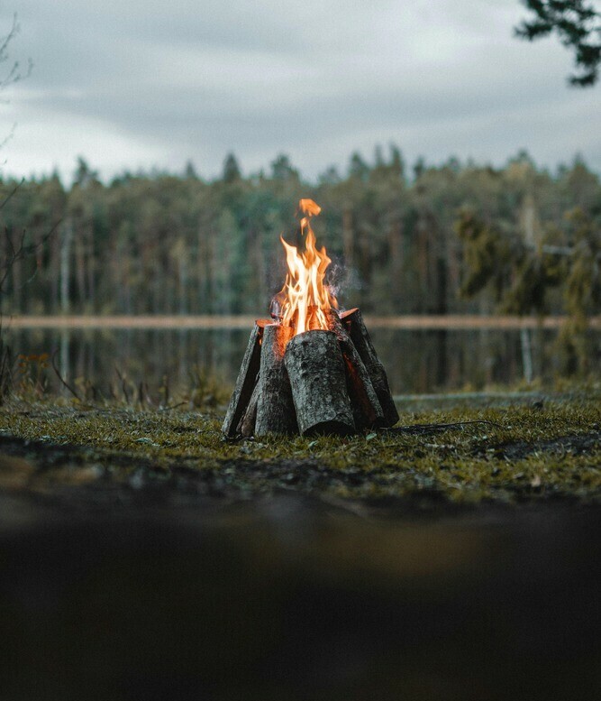Teepee style campfire set close by to a lake surrounded by trees