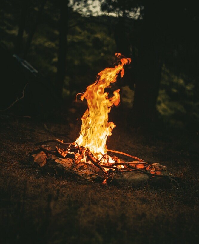 As night sets in a blazing campfire surrounded by rocks lights up the woods