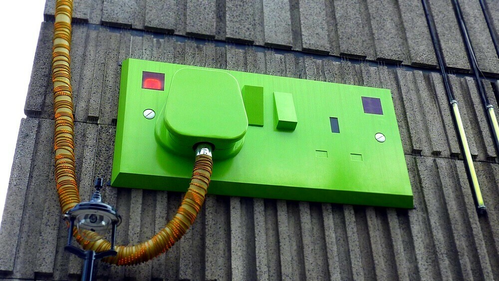 Large artificial green double plug socket  fixed to the outside of a building with a street lamp below