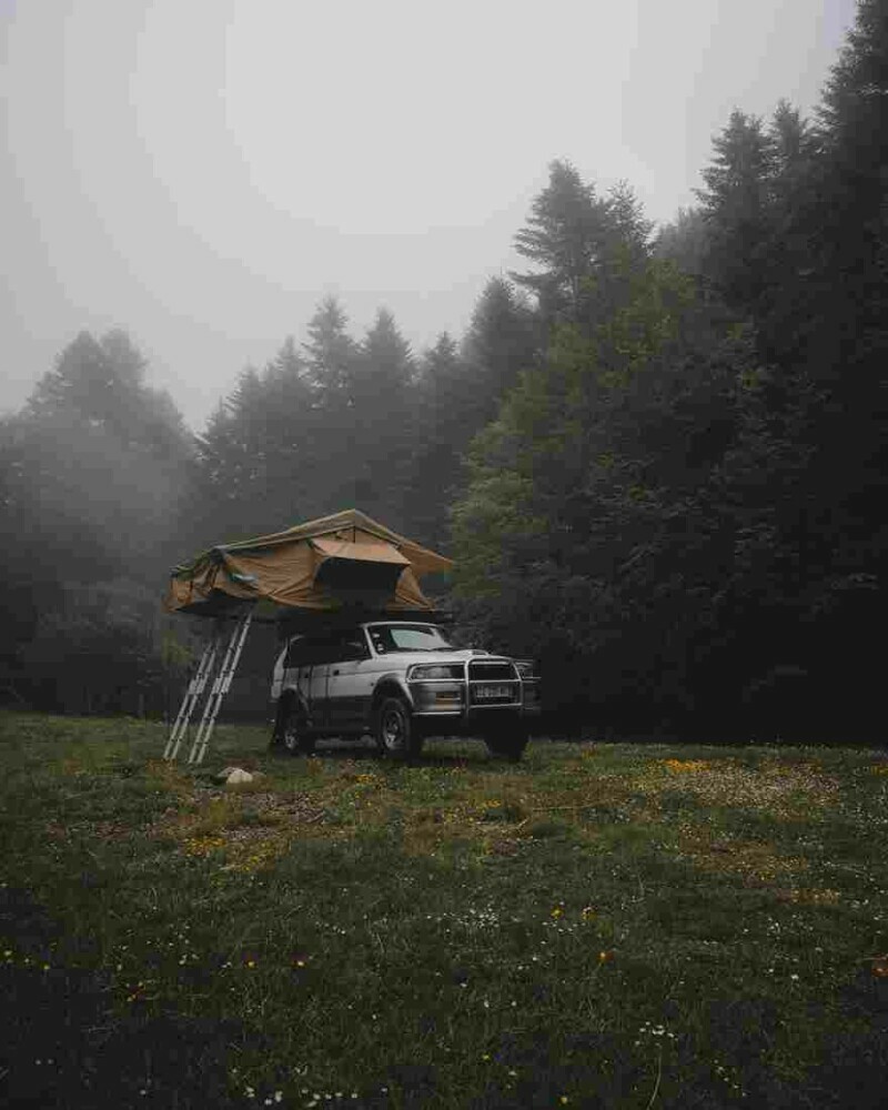 Car with a tent on the roof parked in an opening surrounded by trees on a cold misty morning