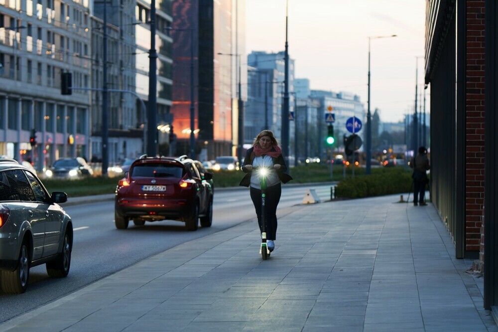 Individual riding their electric scooter on the pavement with their lights on in the city without a helmet