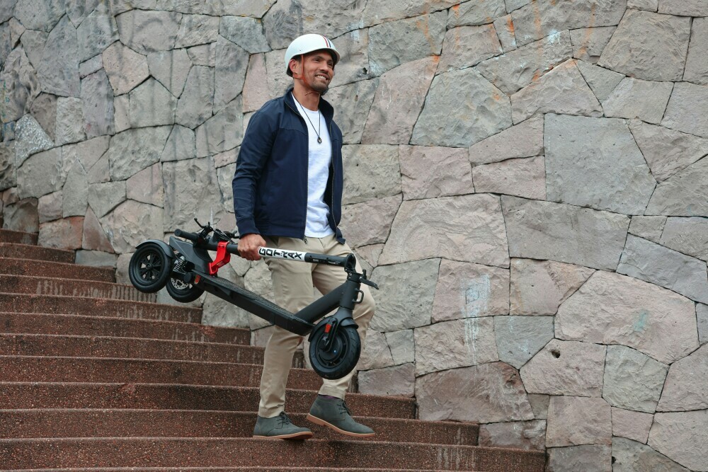 Individual carrying their three wheeled electric scooter down steps whilst wearing a white helmet and smiling