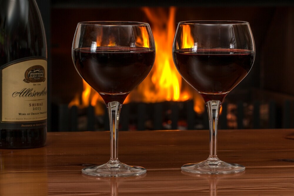 Image of two glasses of red wine with a fireplace in the background