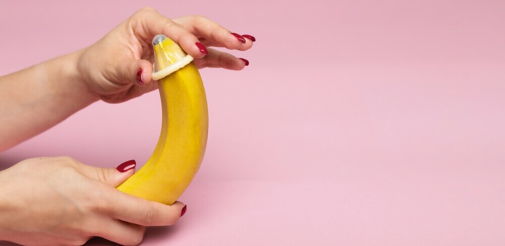 Hands holding a banana with a condom on it