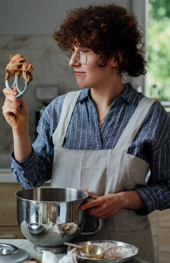 Why Is My Homemade Ice Cream So Hard image 4 woman wearing an apron with kitchen utensil and appliances with mixer blade in hand looking at mixture frosted fusions