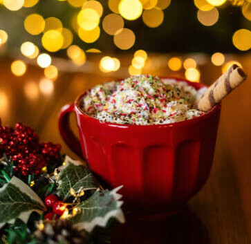 12 Irresistible Christmas Ice Cream Recipes For Your Holiday Table image 6 large red cup filled with ice cream and waffle straws with sprinkles and christmas decor and lights in the background frosted fusions