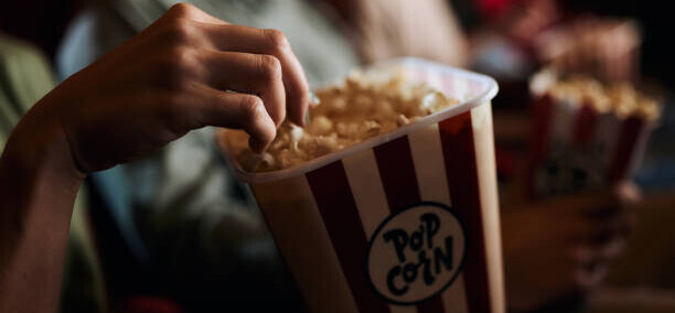 Transform Movie Nights With Delicious Homemade Popcorn Ice Cream image 1 scene at cinema with the focus on a box of popcorn and light from the front screen frosted fusions