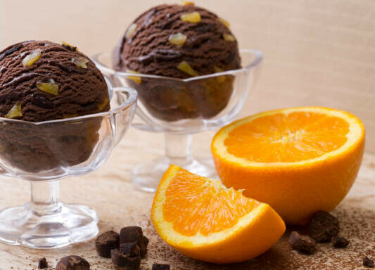 Taste the Nostalgia Terry's Chocolate Orange Homemade Ice Cream image 2 chocolate ice cream scoops in glass dished with an orange halved and chocolate pieces scattered frosted fusions frosted fusions