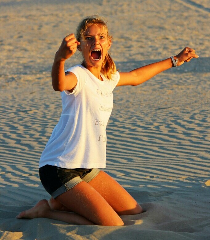 Lady kneeling in the sand on a beach in an expression of victory