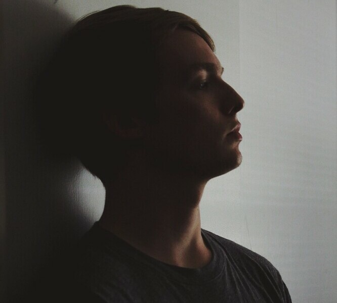 Young guy resting head against a wall looking unhappy