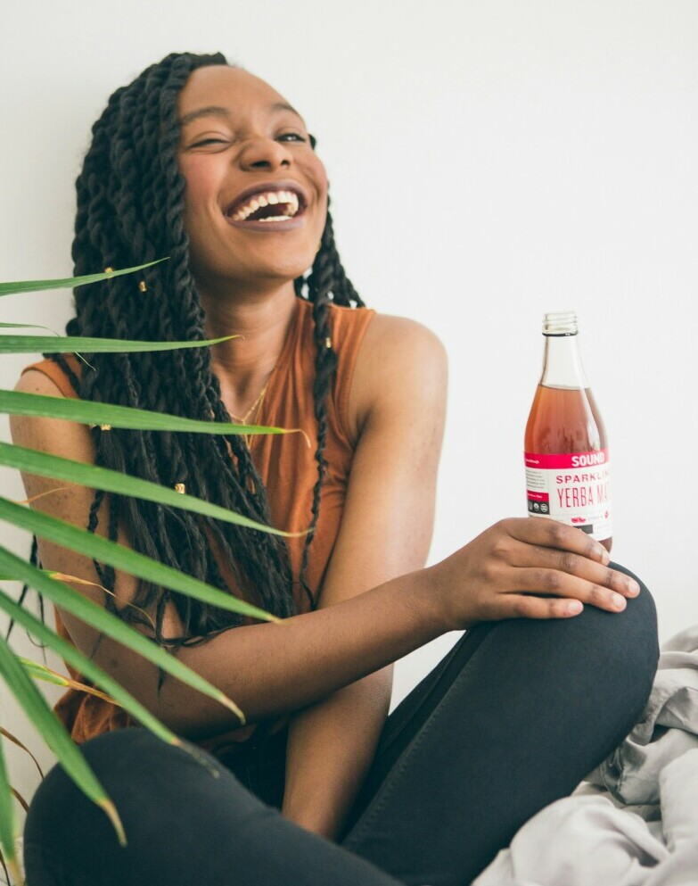 Young lady sitting on the floor laughing with a bottle of drink resting on her knee