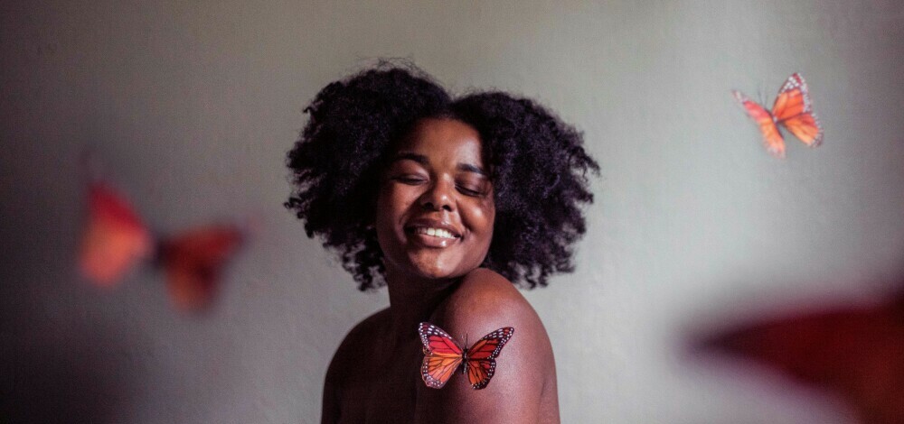 Black lady with beautiful afro smiling and butterflies flying around her