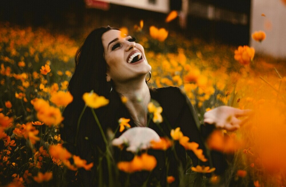 Lady in a field of flowers with outstreched hands laughing