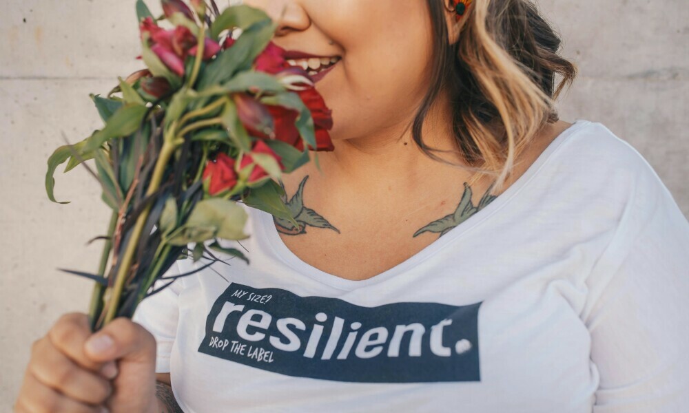 A lady smelling a bunch of flowers in her hands wearing a t-shirt with the word resilience written on it