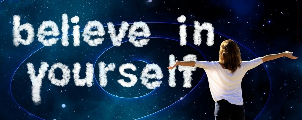 Girl with outstretched arms looking at a board with believe in yourself written on 