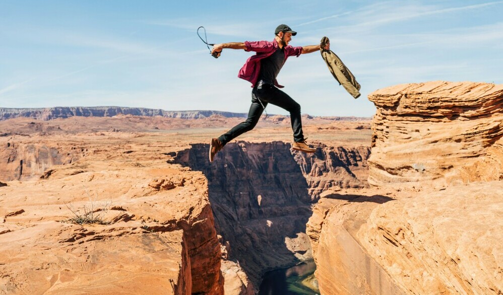 A young man jumping over a crack in a mountain