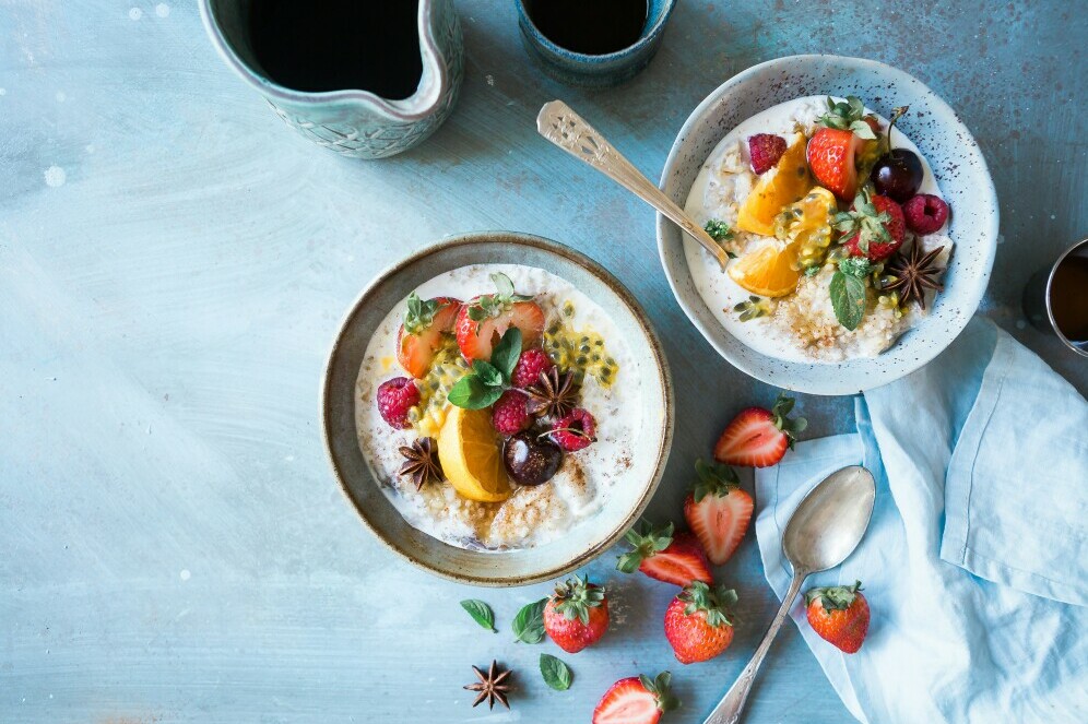 Two Bowls of health breakfast cereal containing fruits and berries and strawbwrries on the table in the foreground