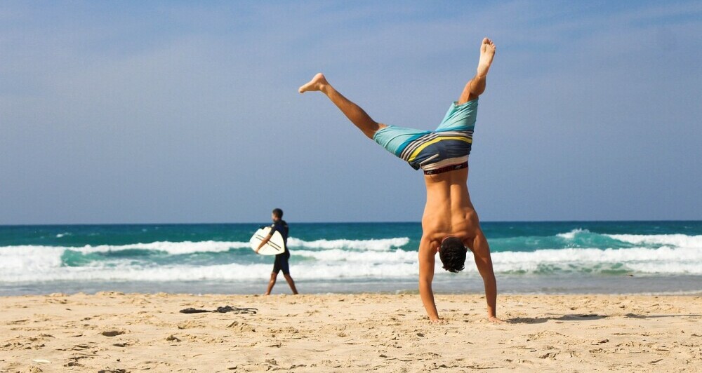 Man doing a handstand on a sandy beach with the Ocean in the distance