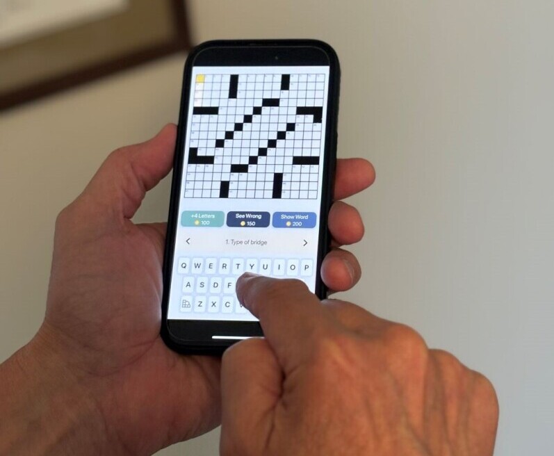 Closeup of hands holding a mobile phone with a blank crossword puzzle on the screen.
