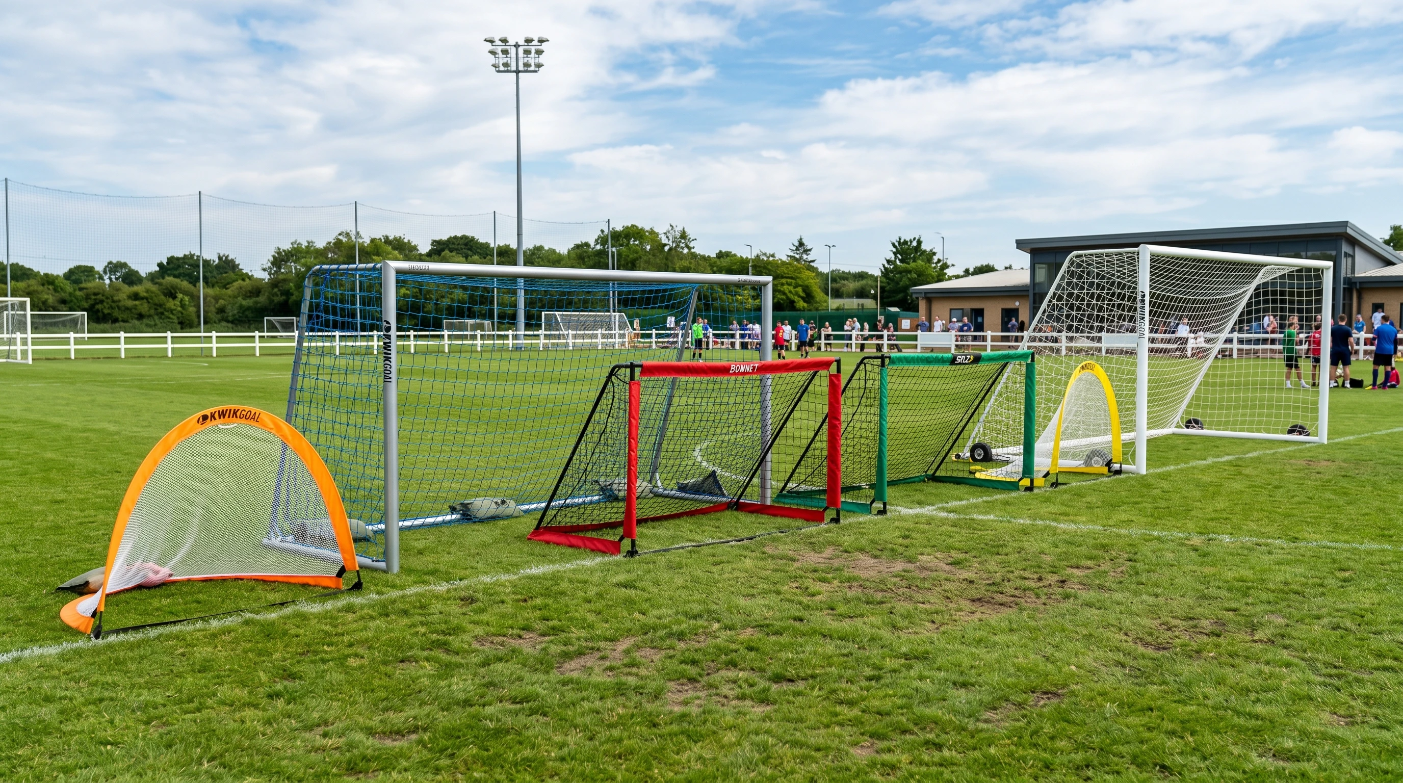 Selection of portable soccer goals arranged on a grassy soccer field, with different sizes and vibrant colors, under a bright sky.