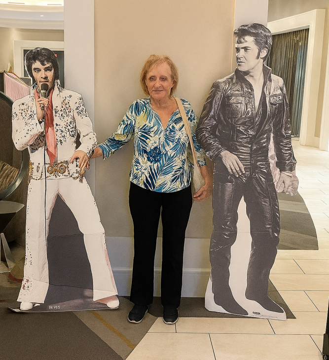 A woman stands between two life-sized cardboard cutouts of Elvis Presley, one in a white rhinestone jumpsuit and the other in black leaA woman stands between two life-sized cardboard cutouts of Elvis Presley, one in a white rhinestone jumpsuit and the other in black leather, inside a hotel lobbyther, inside a hotel lobby