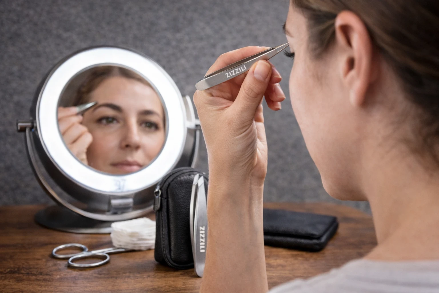 A woman looking into a lighted magnifying mirror using precision tweesers