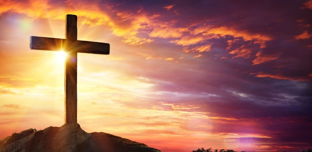 cross on a hill with sun shining through clouds behind it