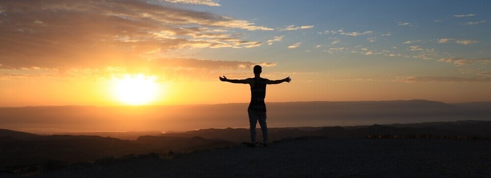 a person stands at the top of a cliff with their arms outstretched to their sides looking at a sunrise