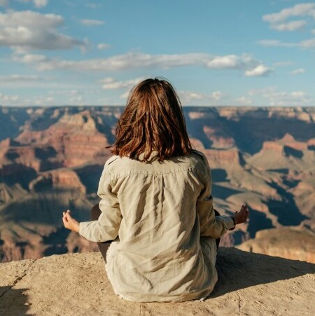 Stress management tools. A woman sitting on a mountain meditating.