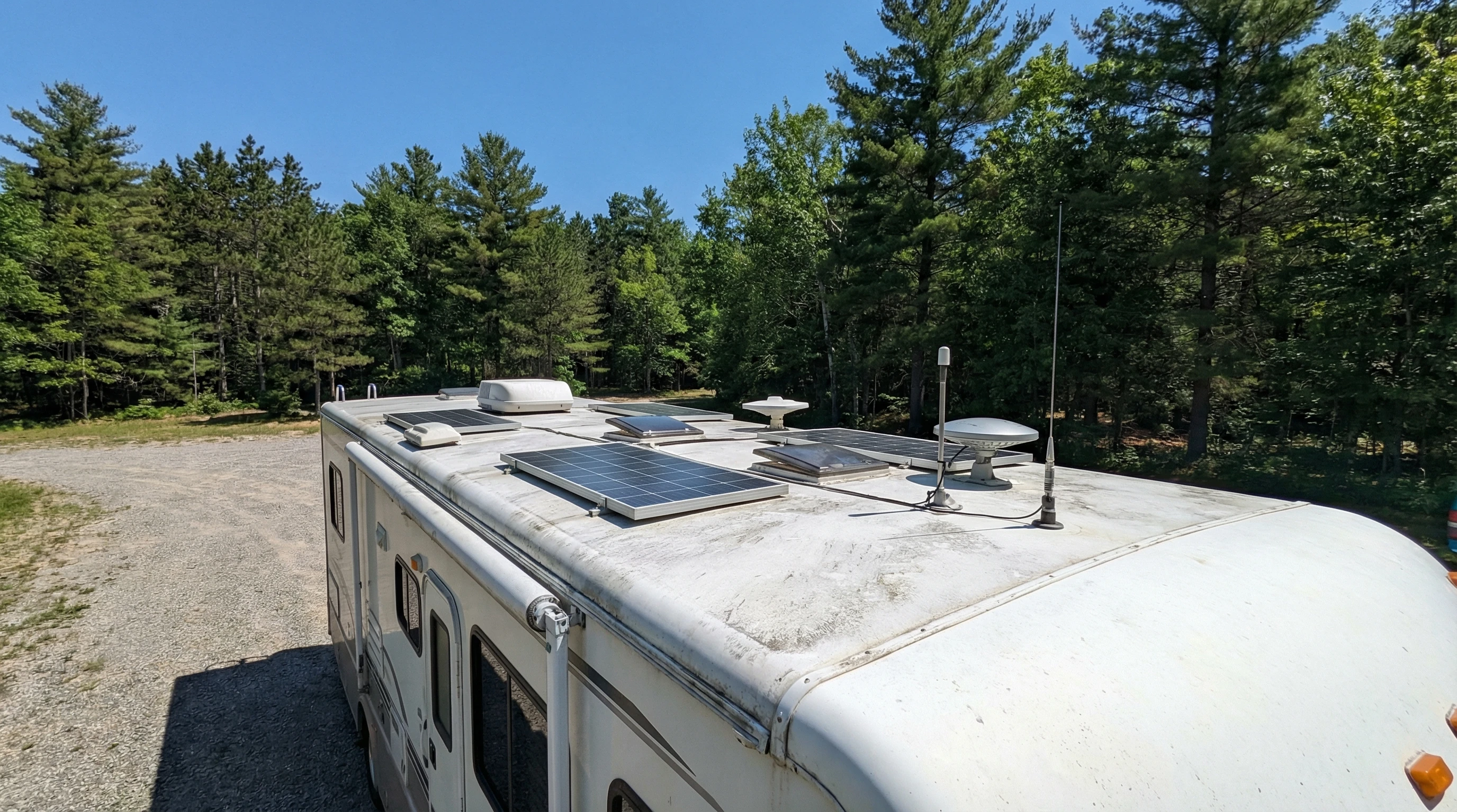 RV parked in snow-covered woods with a satellite dish, radio antennas, and solar panels visible