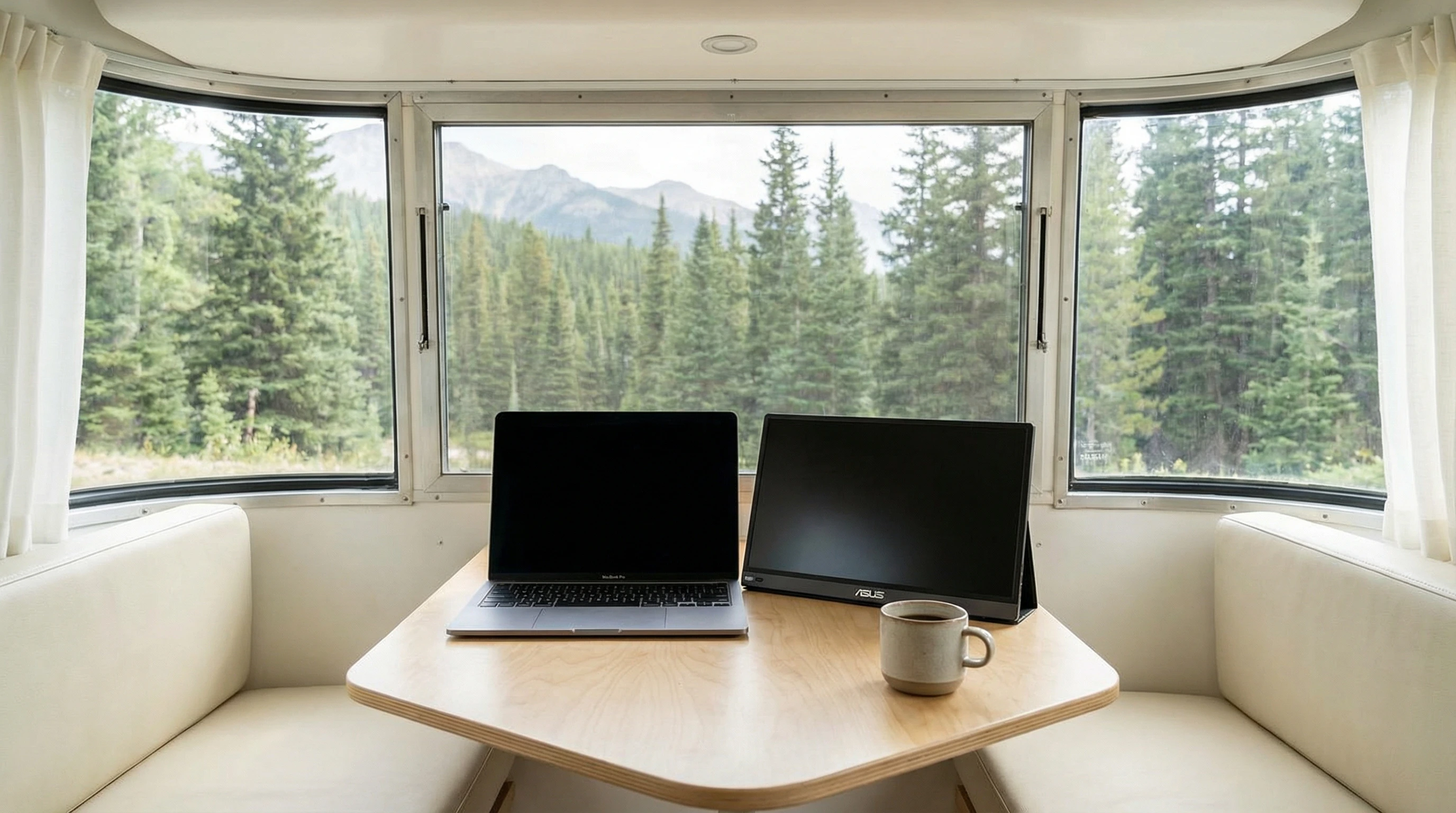 Minimalist RV workspace with laptop, mug, and wireless mouse next to window, forest outside