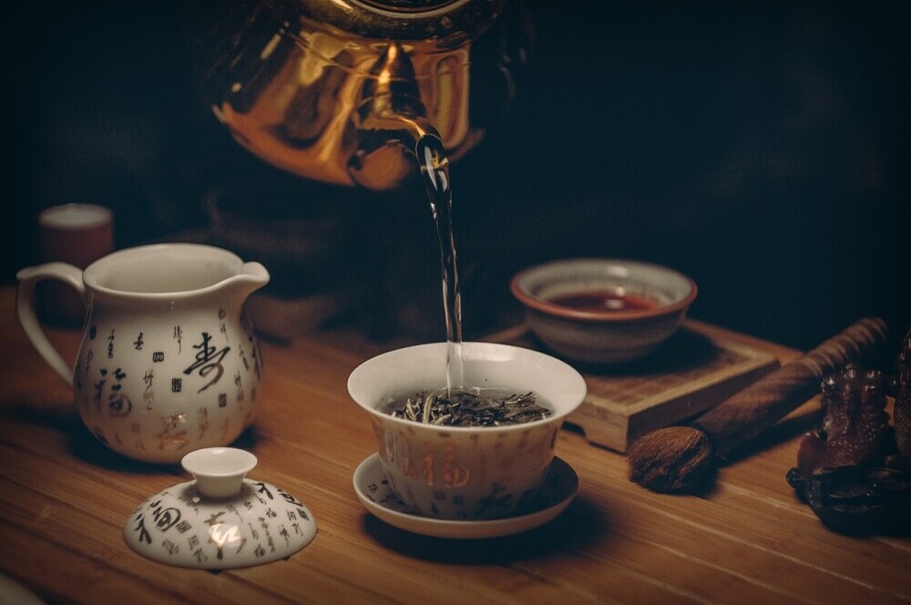 pouring boiling water from a copper kettle into a gaiwan for gongfu style aged white tea brewing