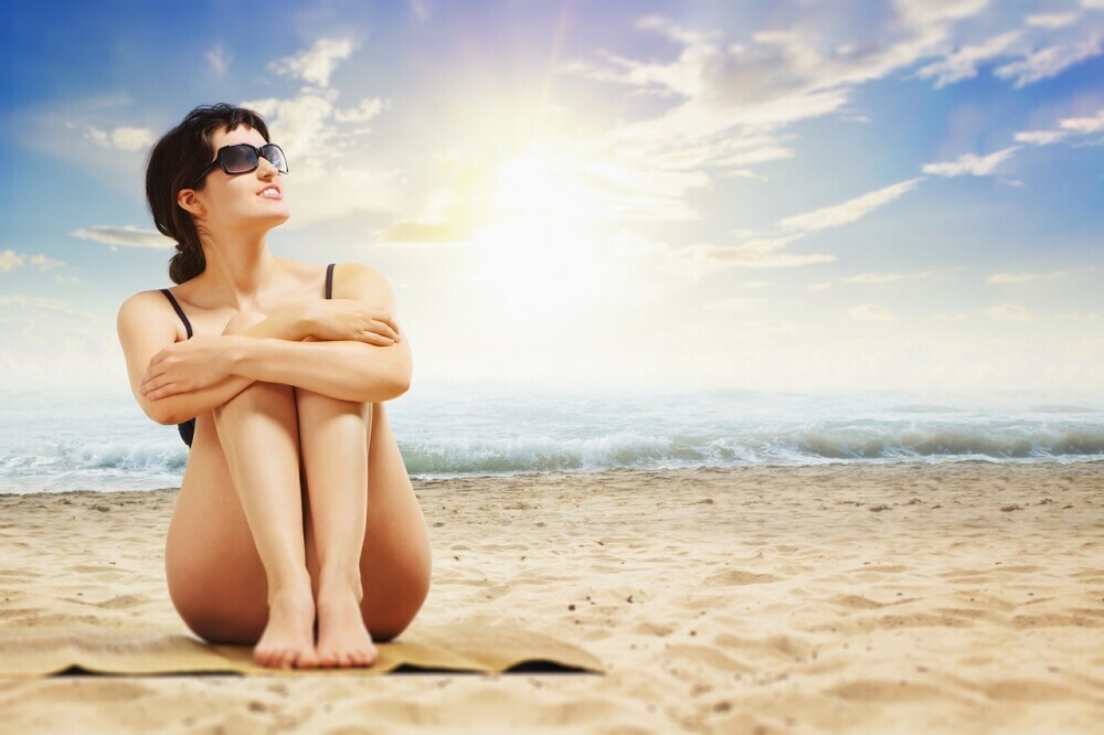 a woman wearing sunglasses sitting on the beach