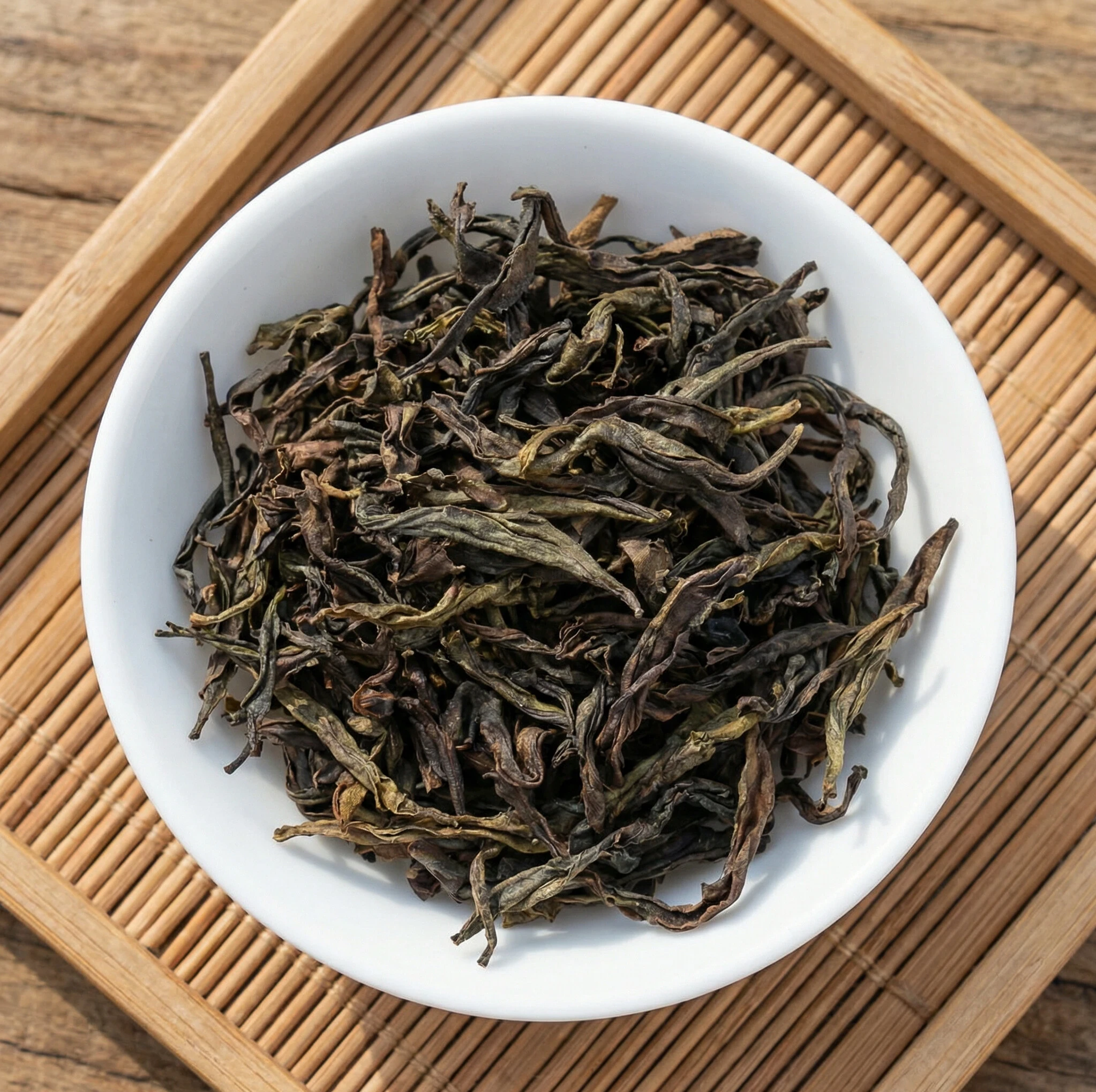 Wuyi Yancha Oolong tea leaves in white bowl on bamboo mat