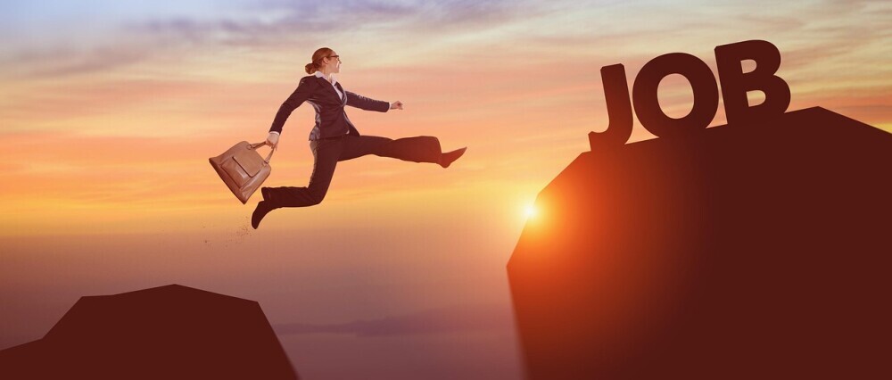 woman in a black suit holding a brief case as she jumps from one mountain peak to the other